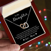 A necklace with two heart-shaped pendants, presented in a box with a Christmas tree decoration in the background.