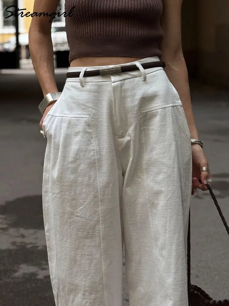 Person wearing a brown top and light-colored wide-leg pants on a street.