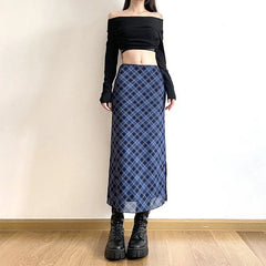 Person wearing a black off-shoulder top and blue plaid skirt against a plain wall.
