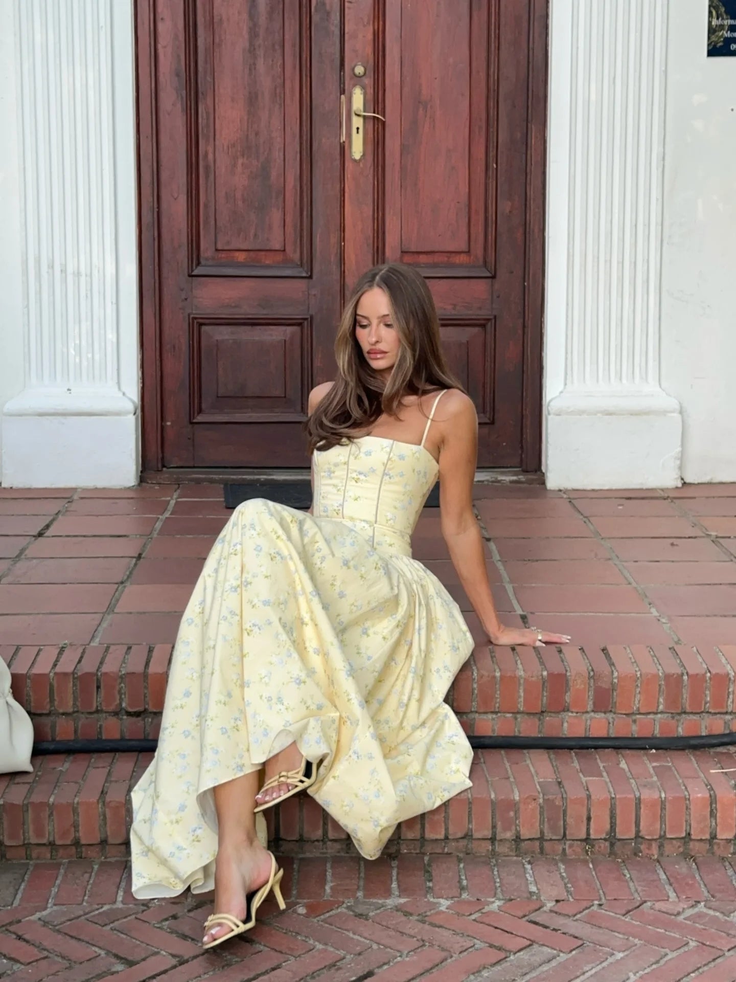 Woman in a yellow dress sitting on steps in front of a wooden door.