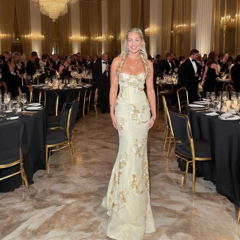 Woman in a formal gown standing in an elegant banquet hall with tables and guests.