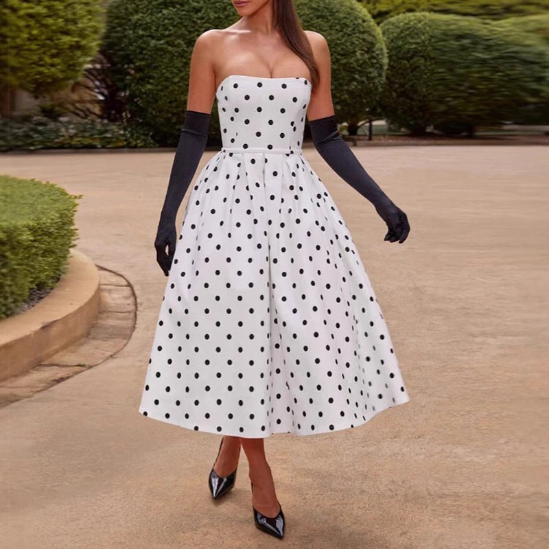 Woman wearing a white strapless dress with black polka dots, black gloves, and black shoes in an outdoor setting.