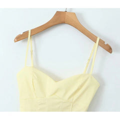 Yellow spaghetti strap top on a wooden hanger against a white background
