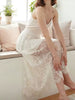 Woman wearing a white lace dress sitting on a couch in a bright room.