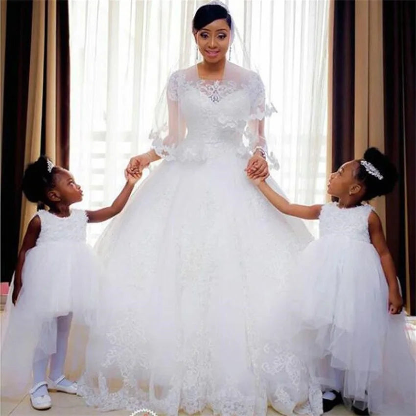 Woman in a white wedding dress holding hands with two young girls in matching white dresses.