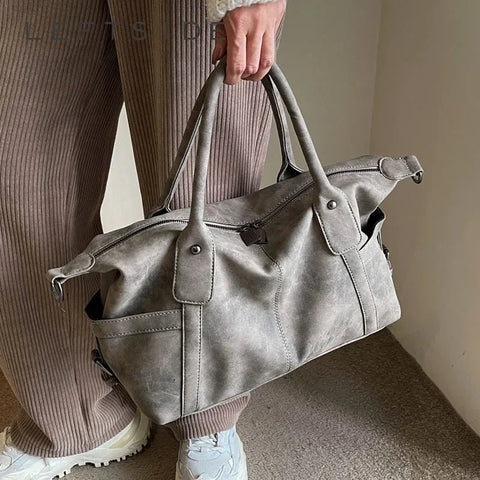 Person holding a gray leather duffel bag with a neutral background