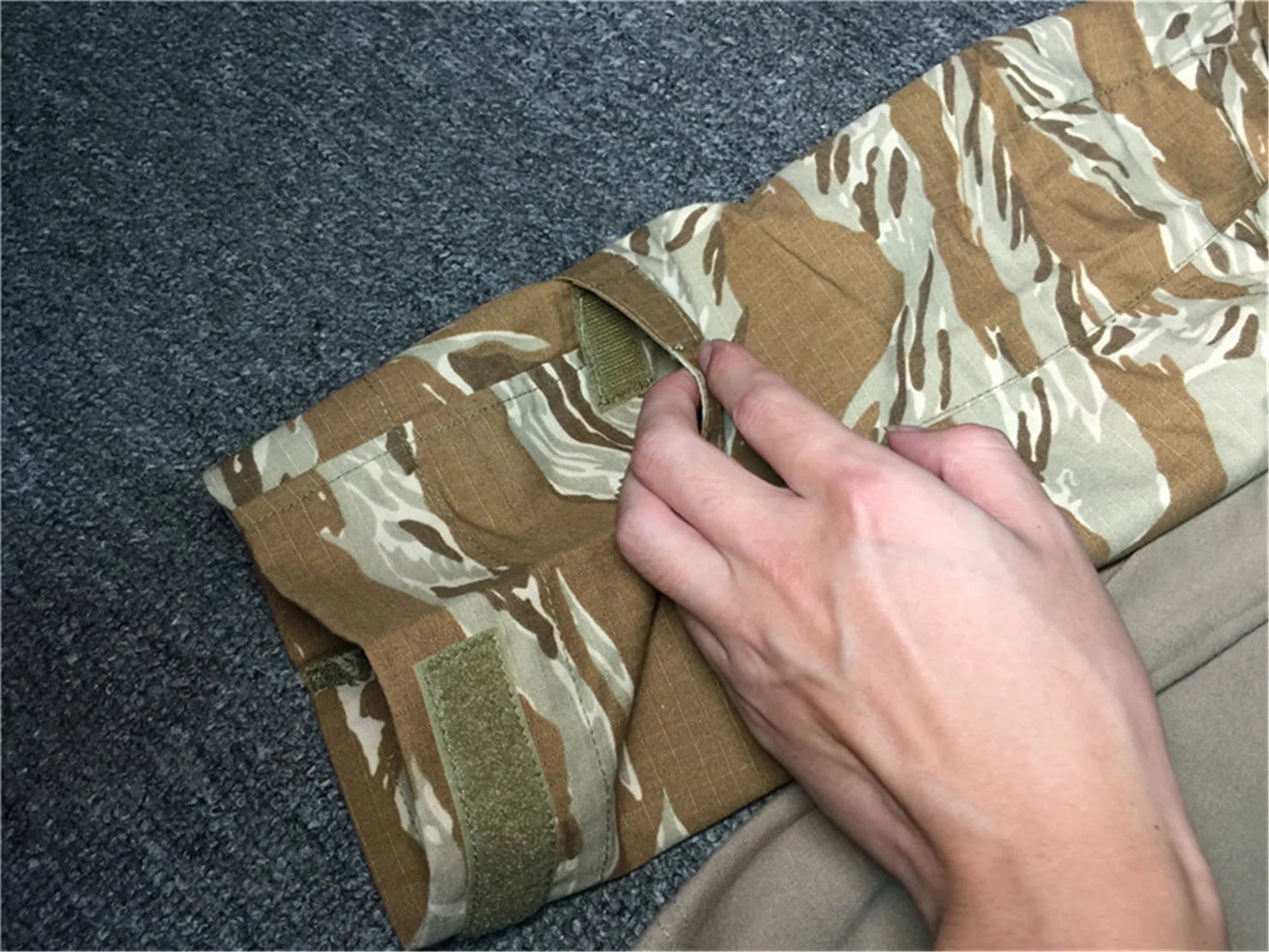 Hand folding a camouflage-patterned blanket on a textured surface