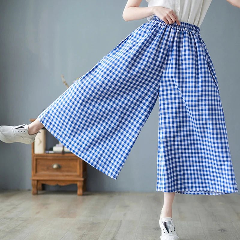 Person wearing a blue and white checkered skirt pants in a room with a wooden cabinet.