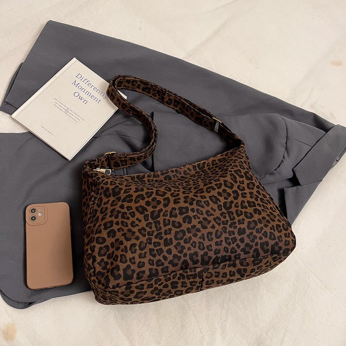 Leopard print handbag with a phone and book on a gray fabric background