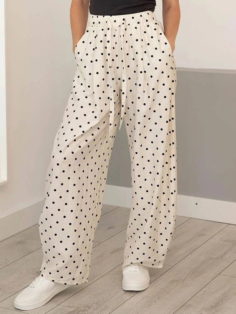 Person wearing white pants with black polka dots and white sneakers in a minimal indoor setting.