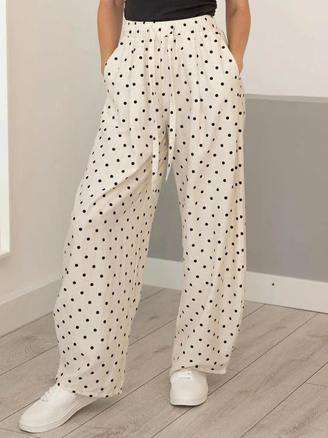 Person wearing white pants with black polka dots and white sneakers in a minimal indoor setting.