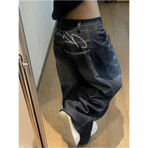 Person wearing oversized dark blue jeans with a visible brand logo on a wooden floor.