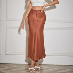 Woman wearing a brown satin skirt against a white wall.