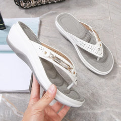 White sandals with gold accents held by a hand on a gray surface