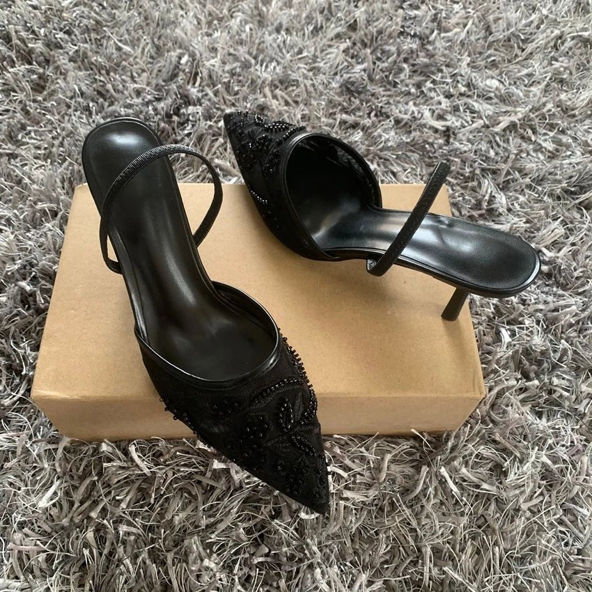 Black high-heeled shoes with embellishments on a beige box against a textured gray background