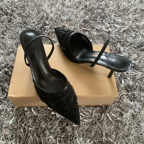 Black high-heeled shoes with embellishments on a beige box against a textured gray background