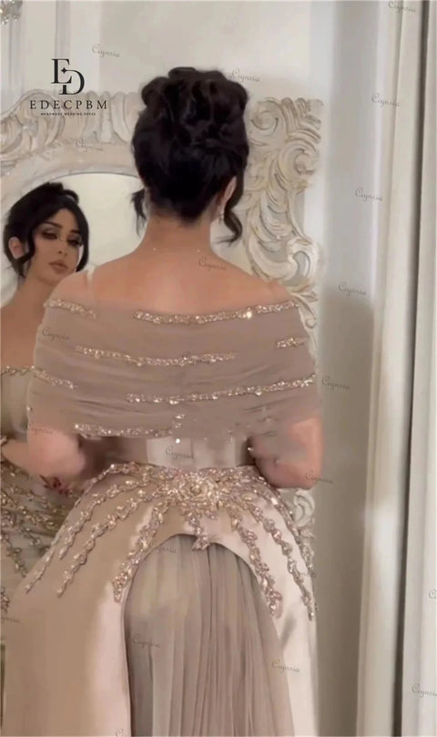 Woman in a beige evening gown with intricate detailing standing in front of a mirror.