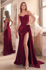 Woman wearing a burgundy evening gown with a high slit in a room with large windows and a white brick wall.