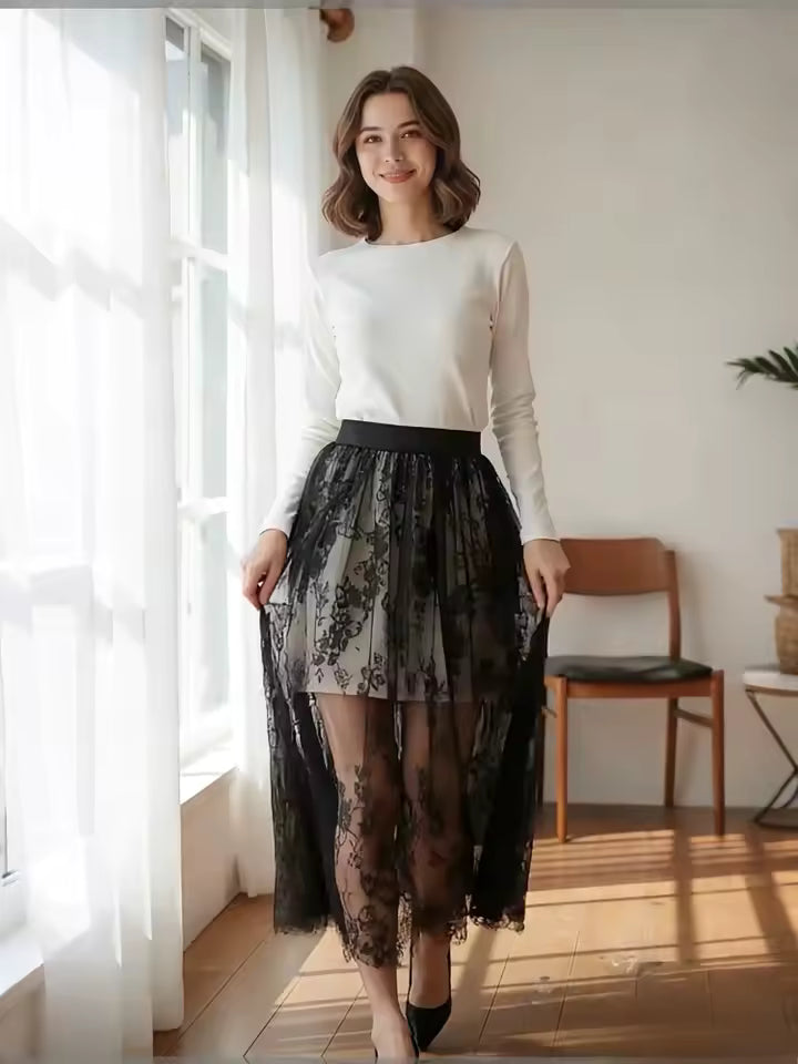 Woman wearing a white long-sleeve top and black lace skirt standing in a room with a window and chair.