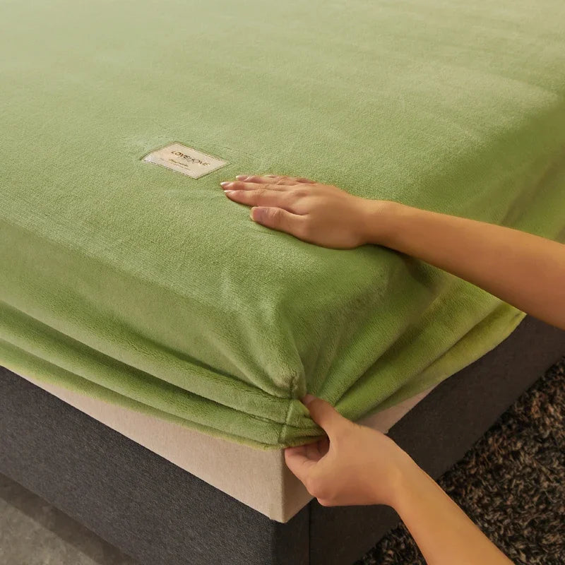 Person adjusting a green fitted sheet on a bed with a visible brand label.