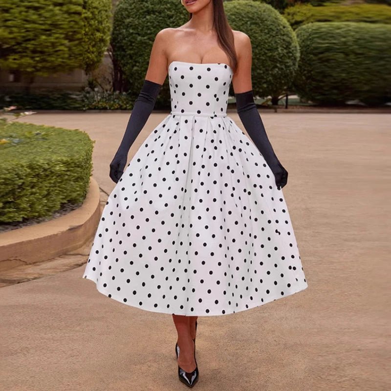 Woman wearing a white strapless dress with black polka dots and navy gloves outdoors.