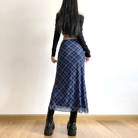 Person wearing a blue plaid skirt and black platform boots against a white wall.
