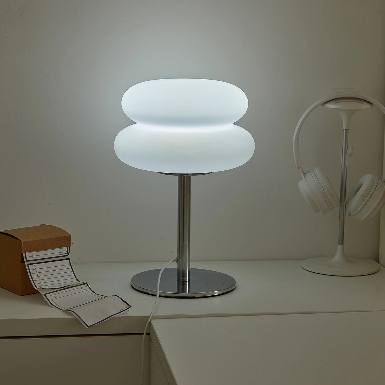 Modern table lamp with a unique design on a desk next to headphones and a box.
