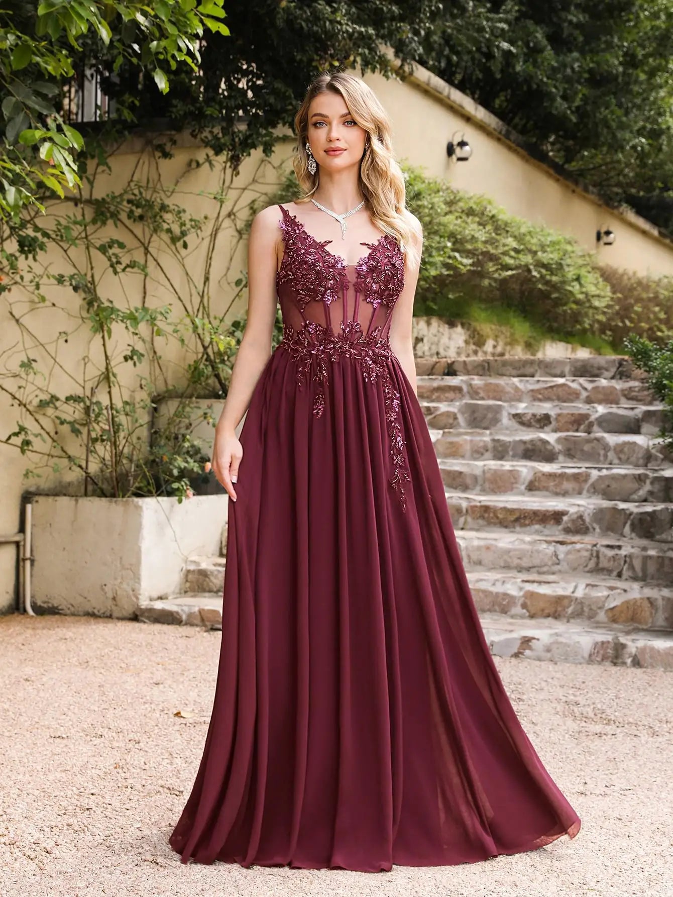 Woman in a burgundy evening gown with lace details standing outdoors.