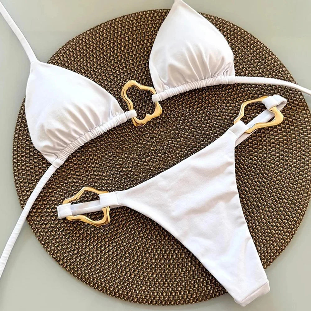 White bikini set with gold hardware on a textured brown surface