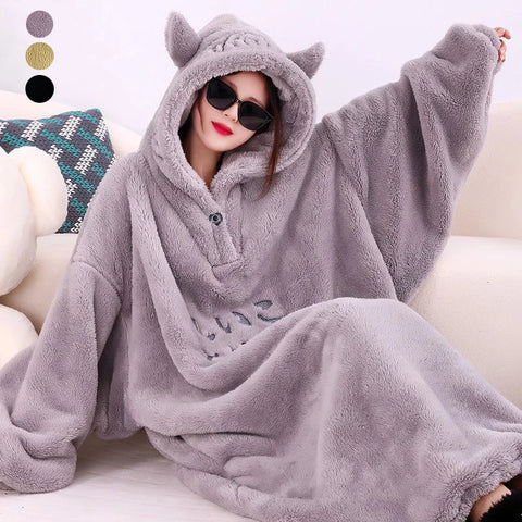 A person wearing a gray fleece oversized blanket robe with a hood, posing on a cozy surface.