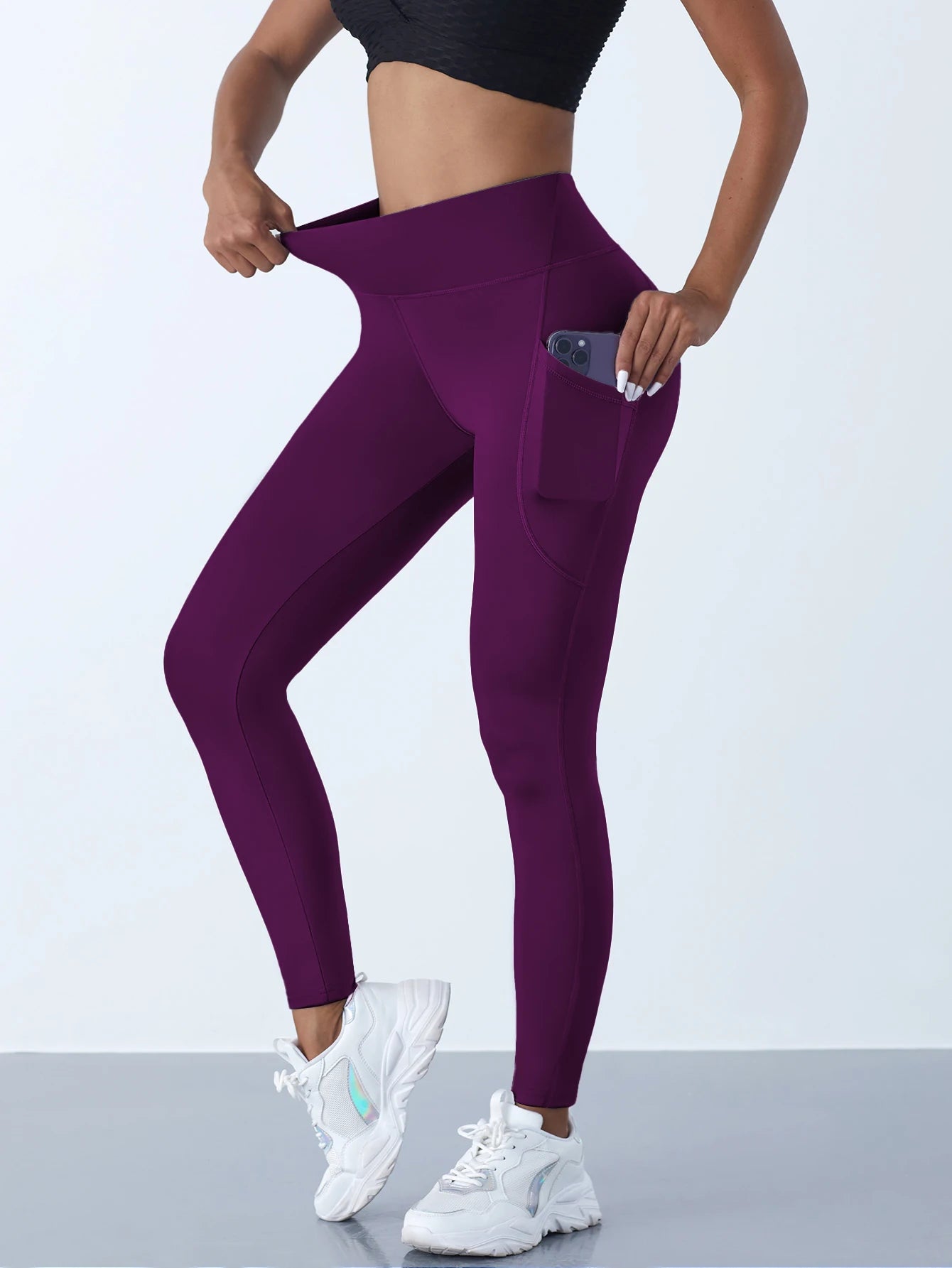 Person wearing purple leggings with a phone in the pocket on a light gray background