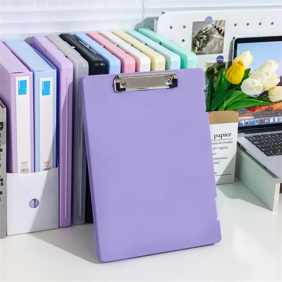 Purple clipboard on a desk with office supplies and a laptop in the background