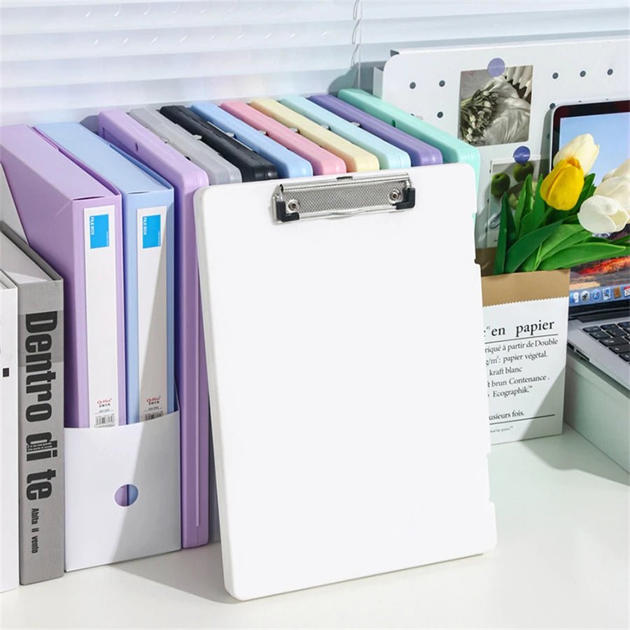 Colorful file folders and a clipboard on a desk with a laptop and flowers in the background.