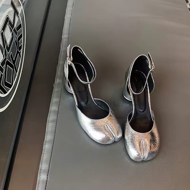 Silver high-heeled shoes on a gray surface with a patterned wall in the background