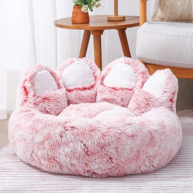 Fluffy pink pet bed with cat ears on a striped rug.