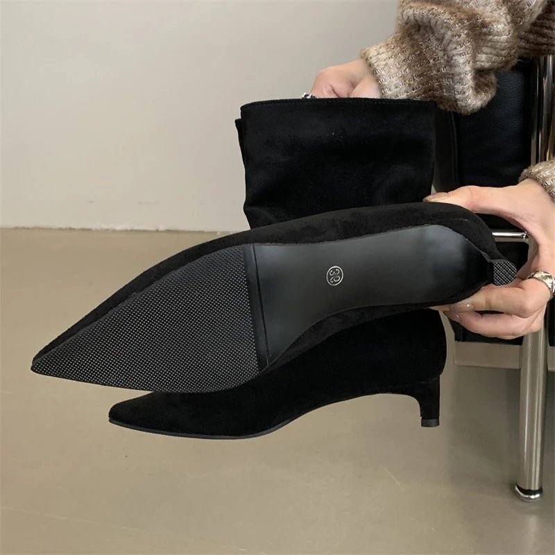 Person wearing black high-heeled shoes with a textured sole, sitting on a chair.