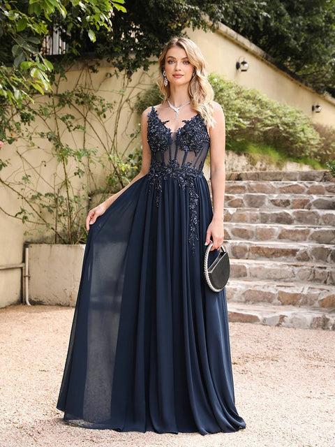 Woman in a navy blue evening gown standing outdoors with steps and greenery in the background