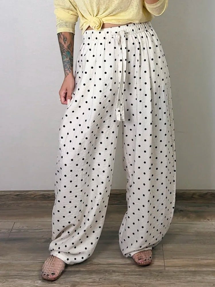 Person wearing white pants with black polka dots and a yellow top against a plain background