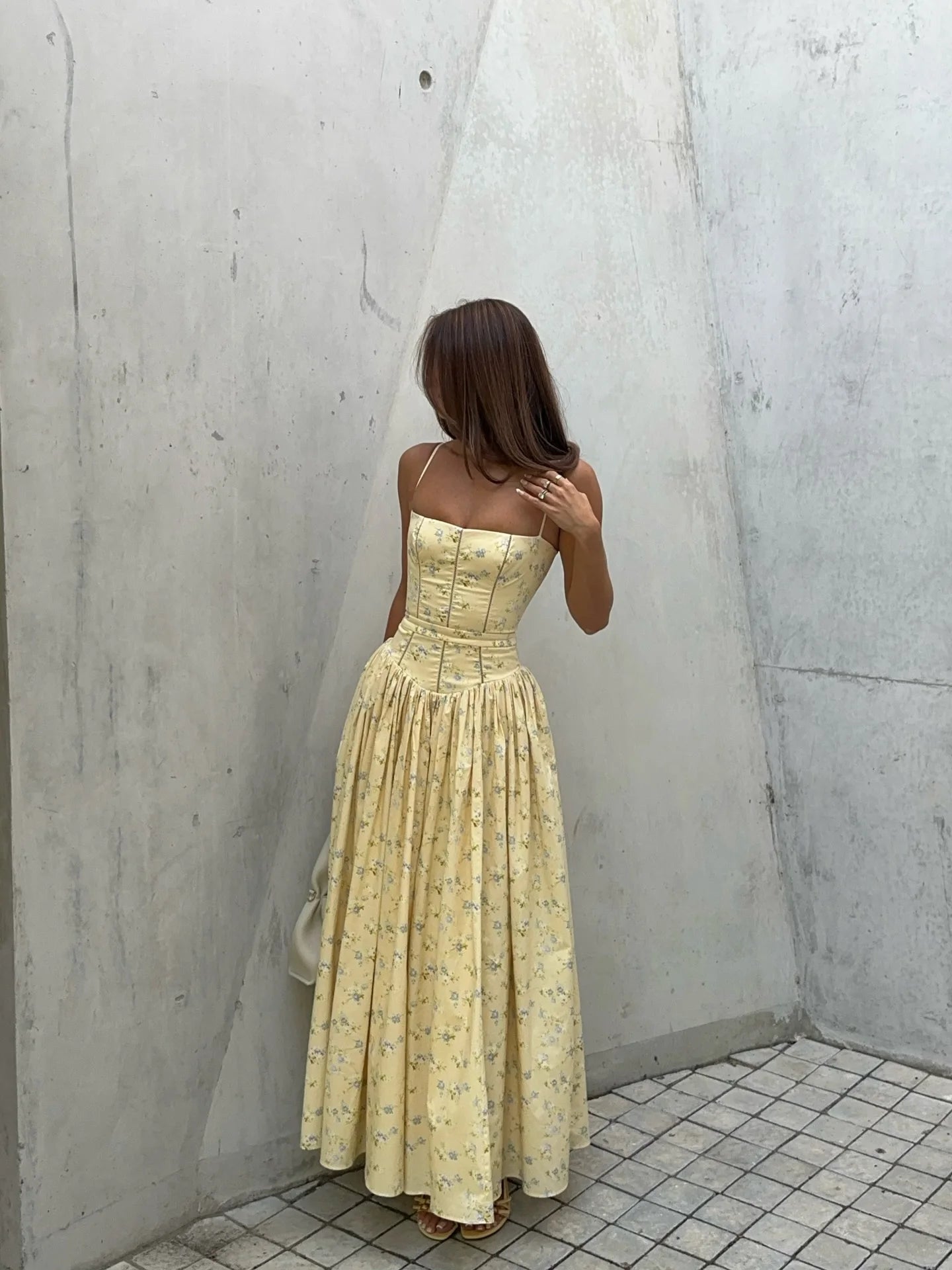 Woman in a yellow dress standing against a gray concrete wall.