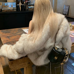 Person wearing a white fur coat sitting at a wooden table in a cafe.