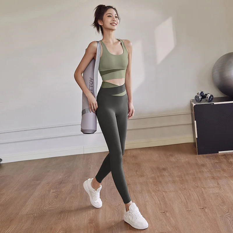 Woman in green athletic wear holding a yoga mat in a room with exercise equipment.