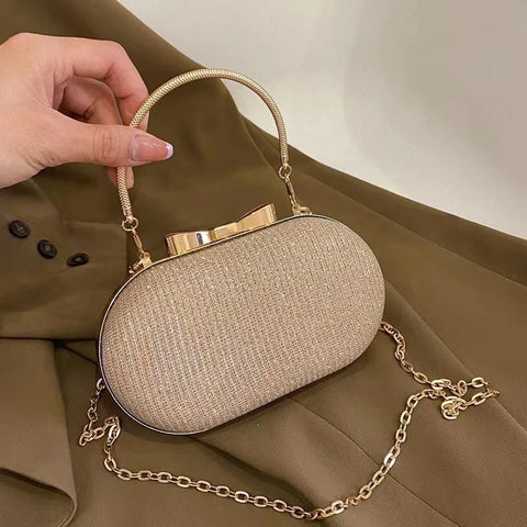 Beige handbag with gold chain strap held by a hand on a beige background
