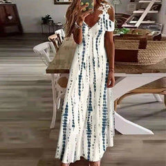 Woman wearing a white dress with blue patterns in a room with wooden flooring and furniture.