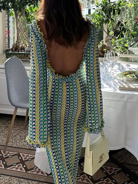 Woman in a patterned dress with a backless design, standing in a room with plants and a table.