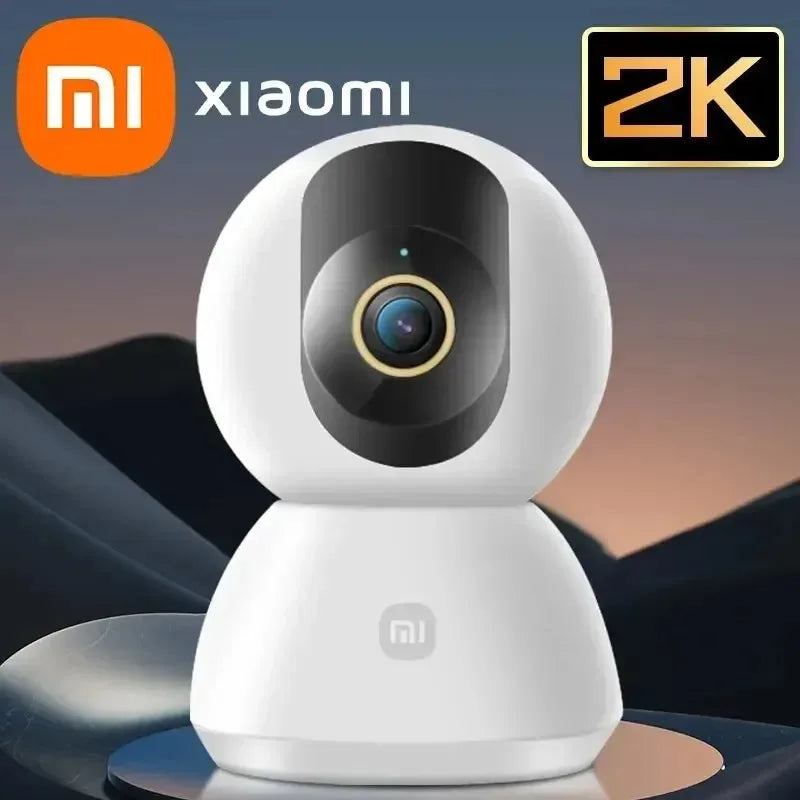 Xiaomi smart camera with 2K resolution on a reflective surface with a blurred landscape background.