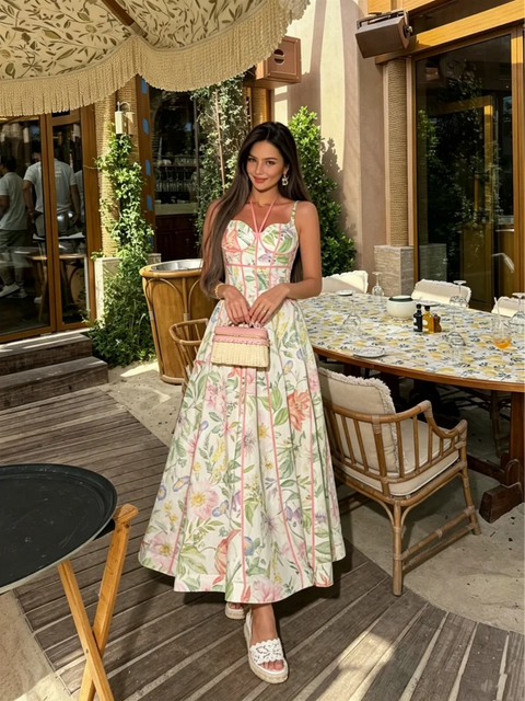 Woman in a floral dress standing in an outdoor setting with tables and chairs.