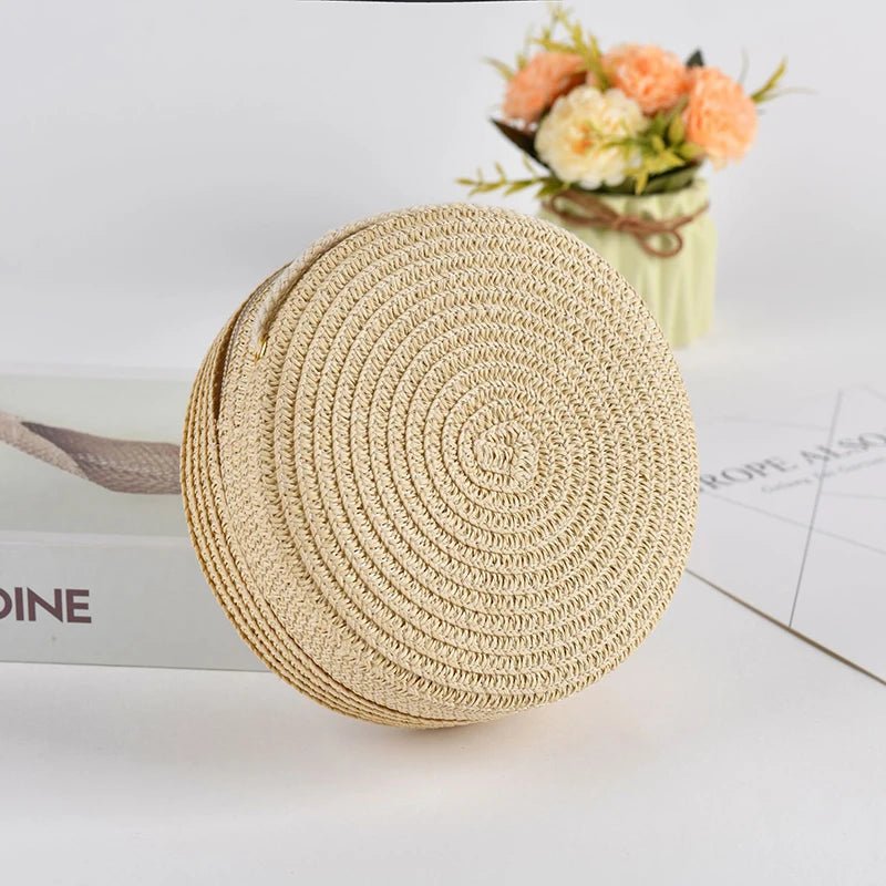 Round woven straw bag on a light surface with flowers in the background