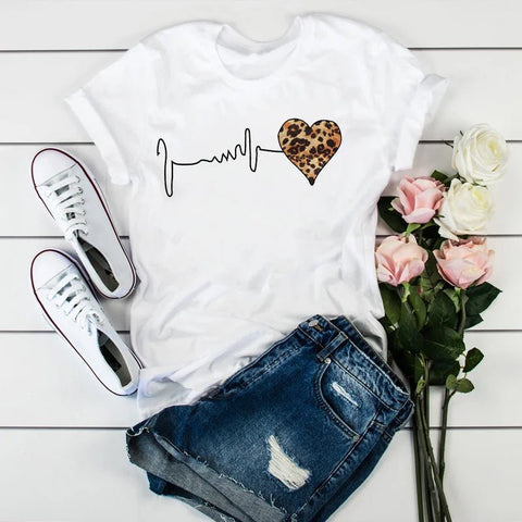 White t-shirt with heart design, white sneakers, denim shorts, and flowers on a wooden surface