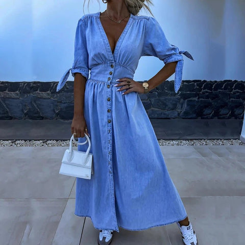 Woman wearing a blue dress with a white handbag in an outdoor setting