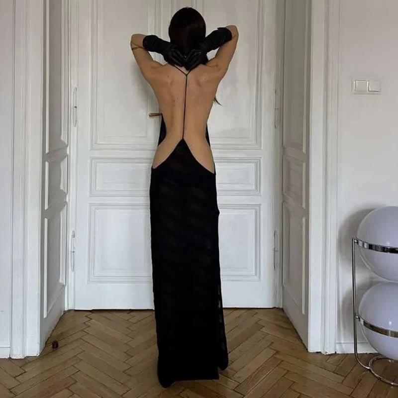 Person wearing a black evening gown with an open back in a room with white walls and wooden floor.